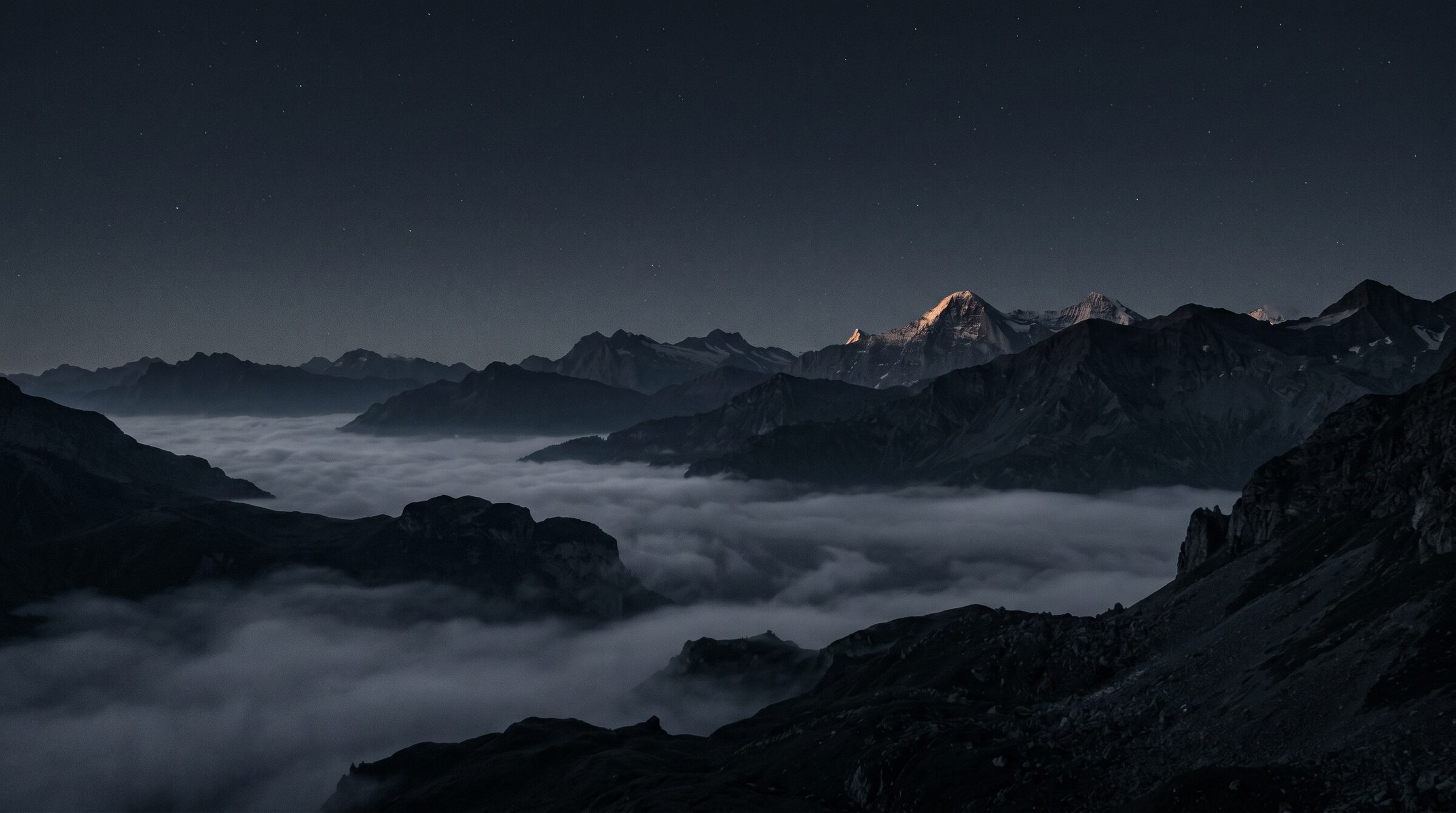 A distant mountain summit catching first light above a sea of fog at pre-dawn